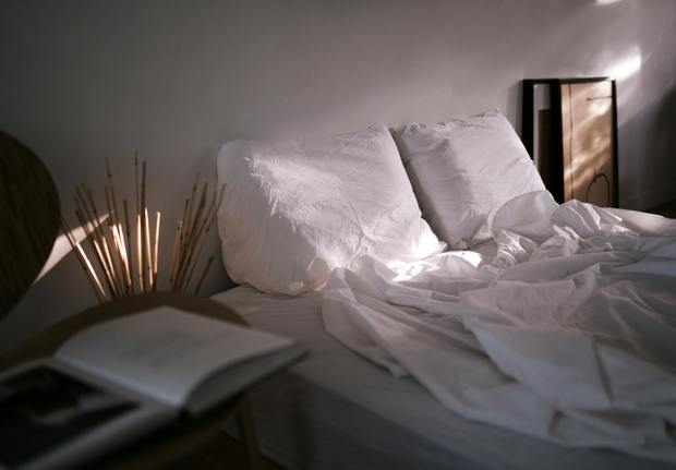A neatly arranged bed with natural fiber bedding including linen pillows and wool blanket